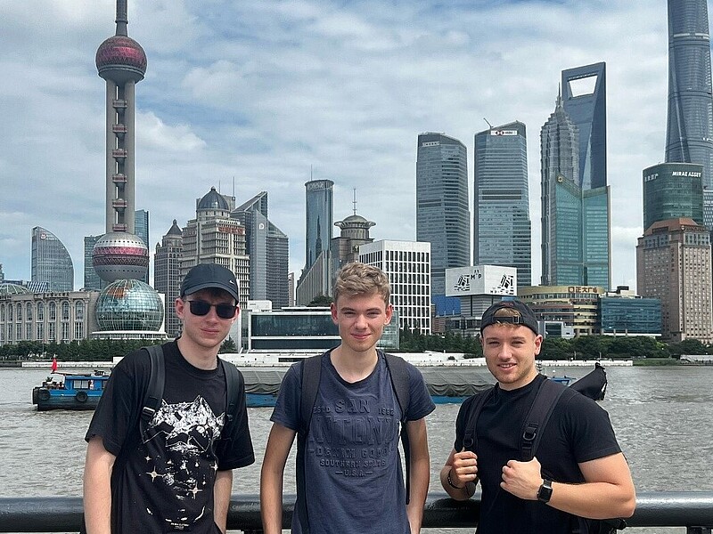 Drei Studenten stehen auf einer Aussichtsplattform vor der Skyline von Shanghai.