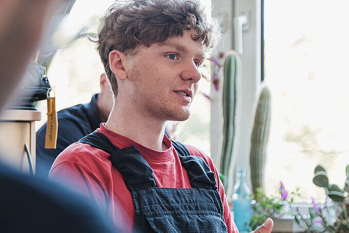 Ein KIA-Student sitzt an einem Tisch und gestikuliert mit seiner Hand.