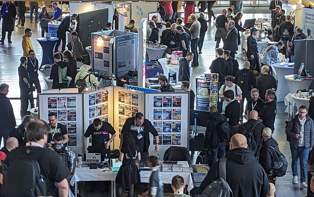 Viele Menschen in einem großen Raum auf einer Messe mit vielen Ständen, Plakaten und Aufstellern
