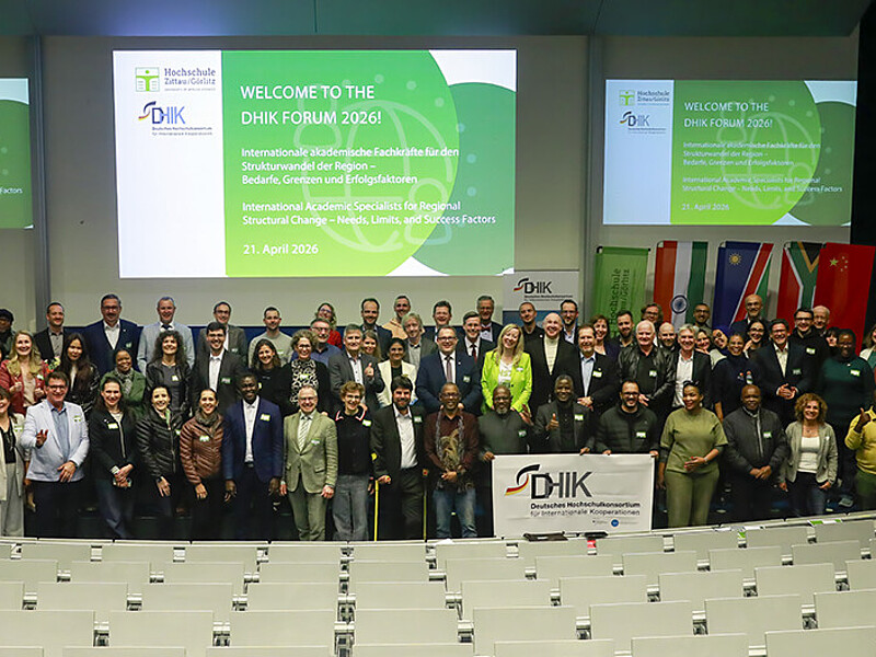 Teilnehmende des Forums des Deutschen Hochschulkonsortiums für Internationale Kooperationen stehen zum Gruppenbild nebeneinander im Audimax vor den Sitzreihen.