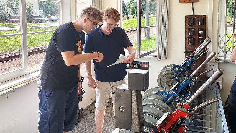 Im mechanischen Stellwerk auf dem Ausbildungsbahnhof Zittau Süd stellen zwei Schüler die Fahrstraße ins Gebirge mit viel Muskelkraft ein und schauen sich dazu Pläne an.