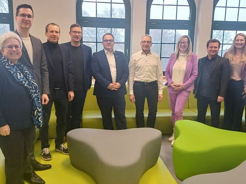 Vertretende der HSZG und Fraunhofer ENAS stehen zwischen grünen Möbeln zum Gruppenbild und lächeln in die Kamera.