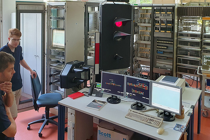 In the faculty's electronic interlocking system, a route is set at the click of a mouse. You can see tables with screens and keyboards and a traffic light system. In the background are cabinets filled with technology.